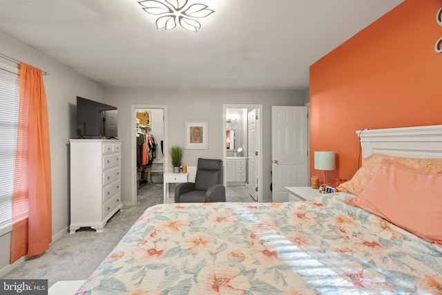 bedroom with a closet, light carpet, baseboards, ensuite bathroom, and a spacious closet