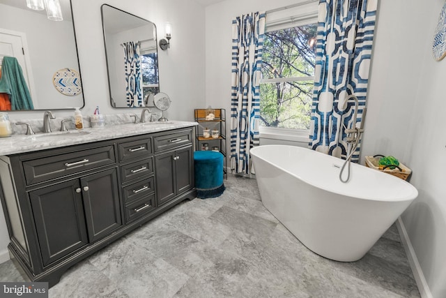 full bath with a sink, marble finish floor, double vanity, and a freestanding bath