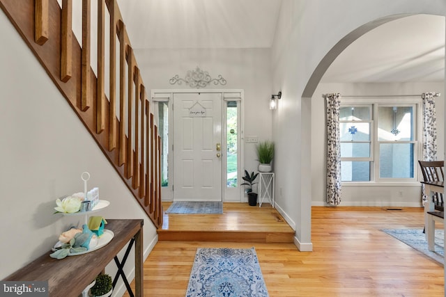 entryway with arched walkways, baseboards, a healthy amount of sunlight, and light wood finished floors