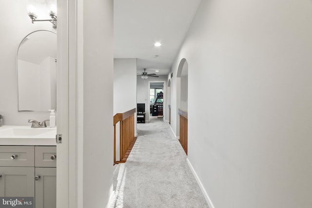 hallway featuring a sink, arched walkways, recessed lighting, and light colored carpet