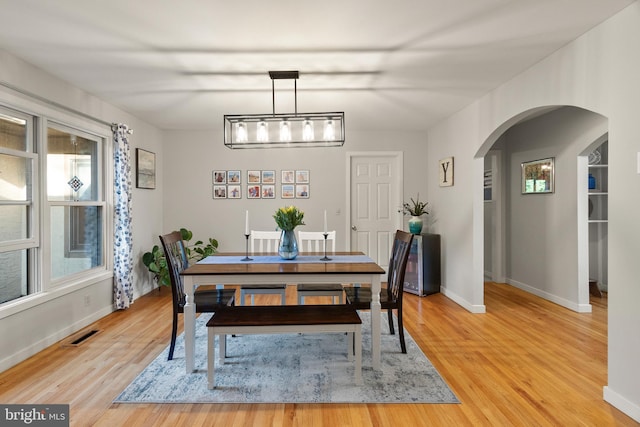 dining area with arched walkways, a healthy amount of sunlight, and light wood-style floors