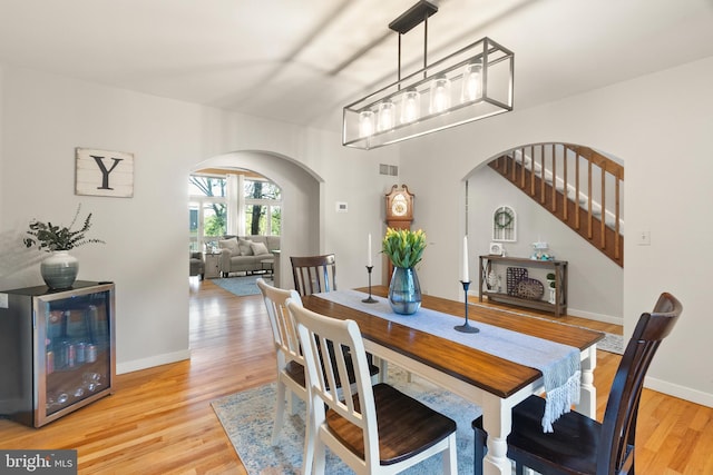 dining space with visible vents, arched walkways, light wood-style flooring, and wine cooler