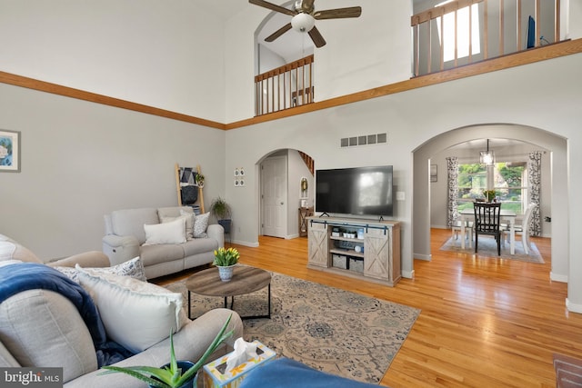 living area featuring arched walkways, ceiling fan, light wood finished floors, and visible vents