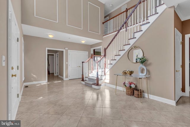 entrance foyer featuring a towering ceiling, crown molding, stairway, baseboards, and tile patterned floors