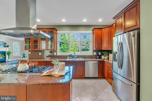 kitchen featuring decorative backsplash, island range hood, a sink, dark stone countertops, and appliances with stainless steel finishes