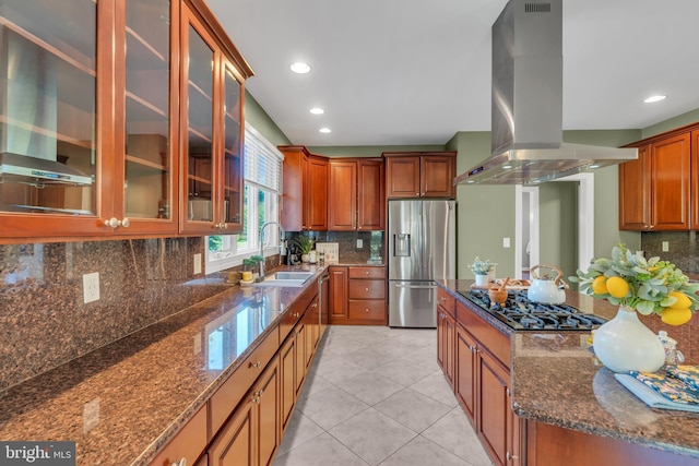 kitchen with gas cooktop, a sink, dark stone countertops, island range hood, and stainless steel refrigerator with ice dispenser