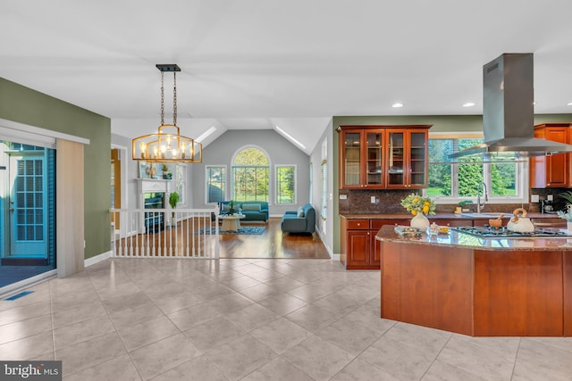 kitchen with a sink, stone countertops, island range hood, backsplash, and glass insert cabinets