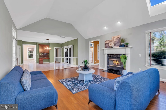 living room with visible vents, a high end fireplace, lofted ceiling with skylight, and wood finished floors
