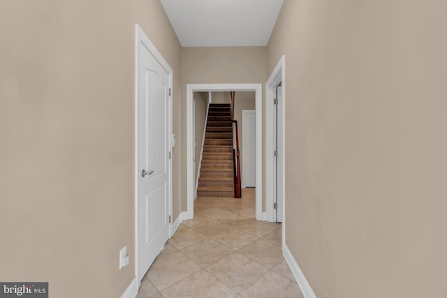 corridor featuring baseboards, stairs, and light tile patterned flooring