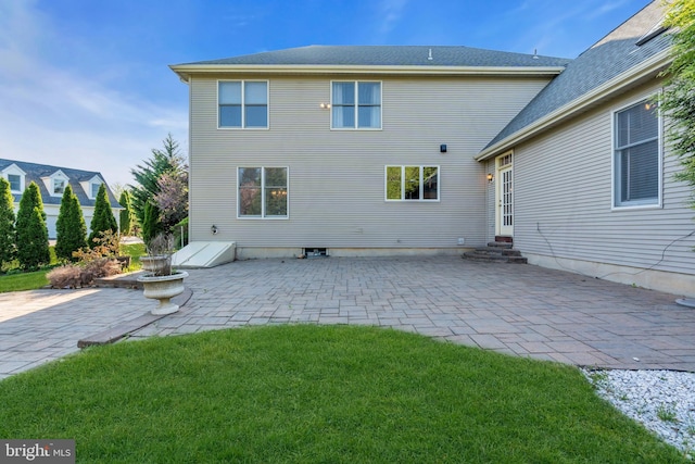back of property with entry steps, a patio, a lawn, and roof with shingles
