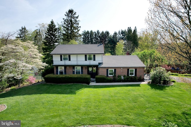 view of front of house featuring brick siding, a chimney, a balcony, and a front yard