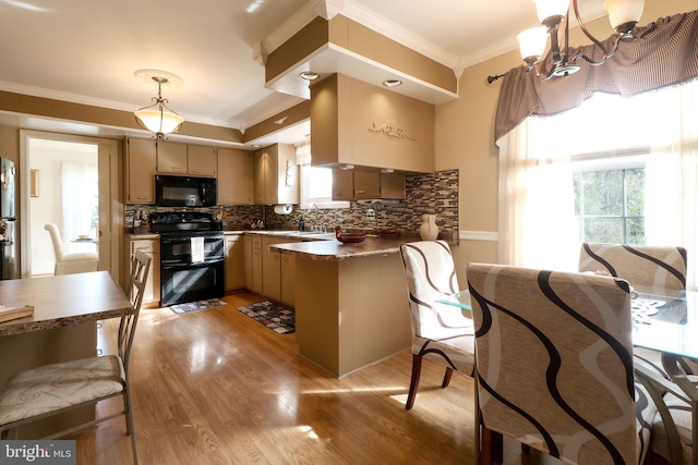 kitchen with a peninsula, light wood-type flooring, backsplash, ornamental molding, and black appliances