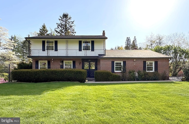 traditional-style house with a chimney, brick siding, a balcony, and a front yard