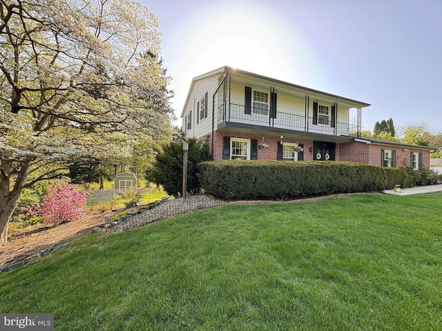 view of front of property featuring an outdoor structure, a balcony, a front yard, brick siding, and a storage shed