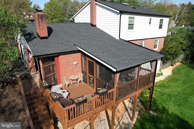 rear view of house with a chimney, roof with shingles, a lawn, a wooden deck, and a sunroom