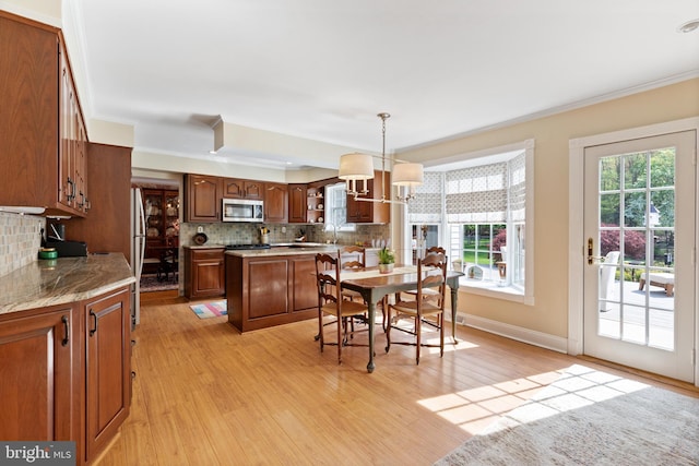 kitchen featuring light wood-style floors, tasteful backsplash, stainless steel microwave, an inviting chandelier, and ornamental molding