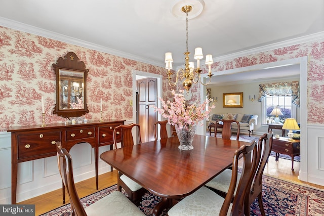 dining space featuring crown molding, a wainscoted wall, a notable chandelier, and wallpapered walls
