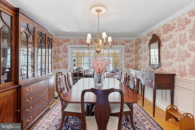 dining room with wallpapered walls, a chandelier, wood finished floors, and a wainscoted wall