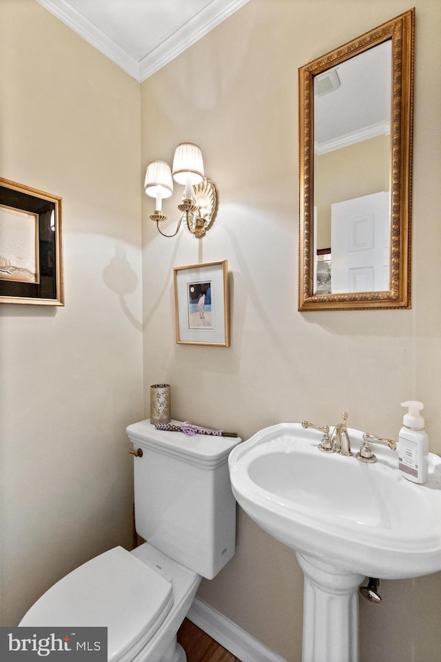 half bathroom with toilet, baseboards, ornamental molding, and a sink