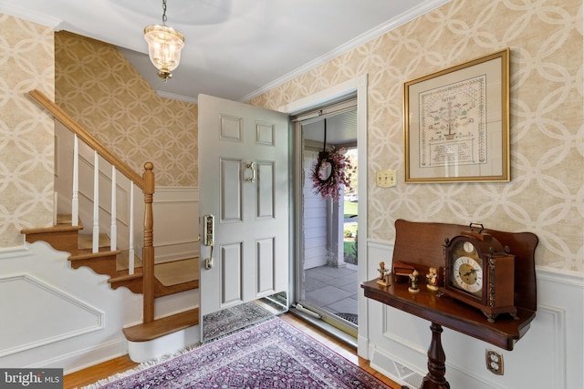 foyer with ornamental molding, stairs, a wainscoted wall, and wallpapered walls