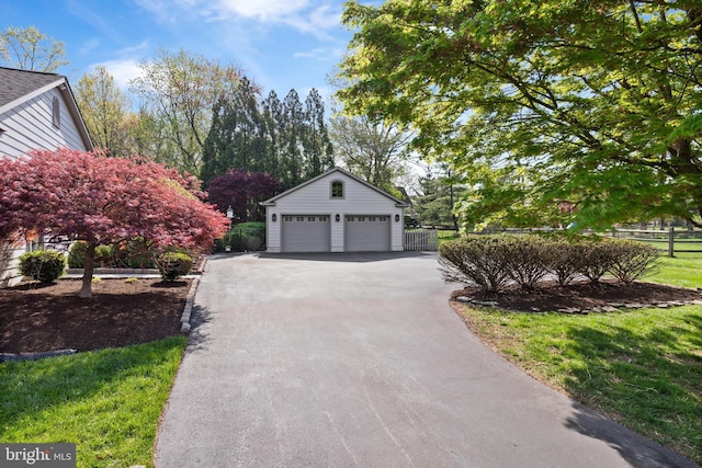 view of side of property with aphalt driveway, fence, an outbuilding, and a garage