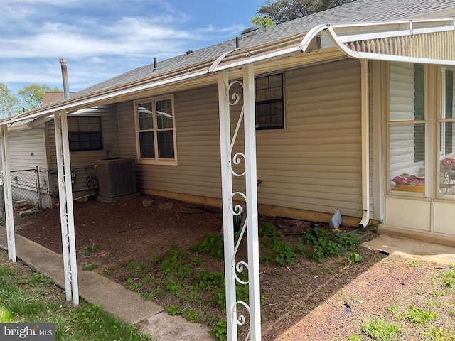 exterior space featuring central AC, fence, and roof with shingles