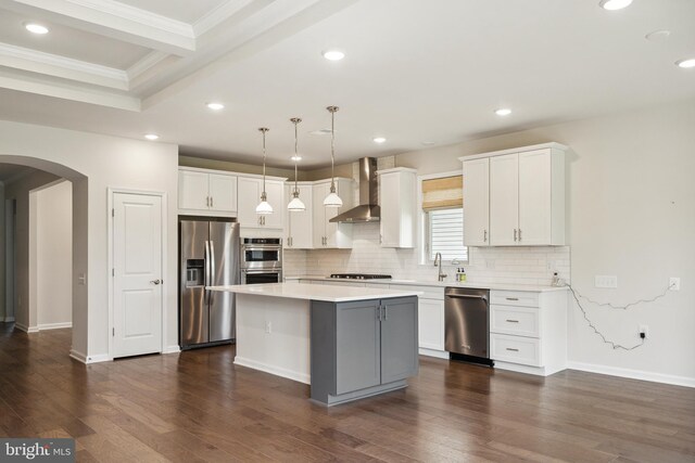 kitchen with wall chimney range hood, decorative backsplash, arched walkways, stainless steel appliances, and dark wood-type flooring