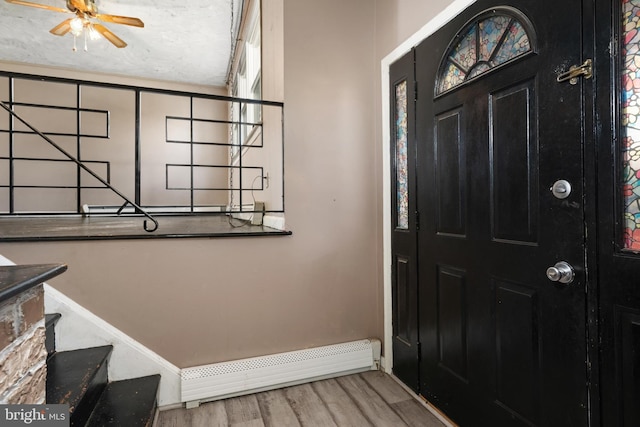 foyer entrance featuring baseboards, ceiling fan, wood finished floors, and a baseboard radiator