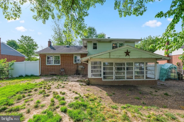 back of property with fence, a chimney, a sunroom, and brick siding
