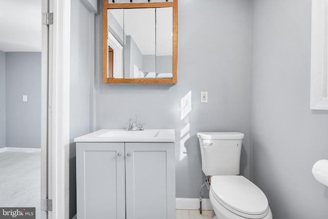 half bathroom with baseboards, vanity, and toilet