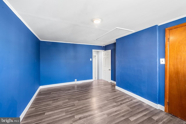 unfurnished room featuring crown molding, baseboards, wood finished floors, and attic access