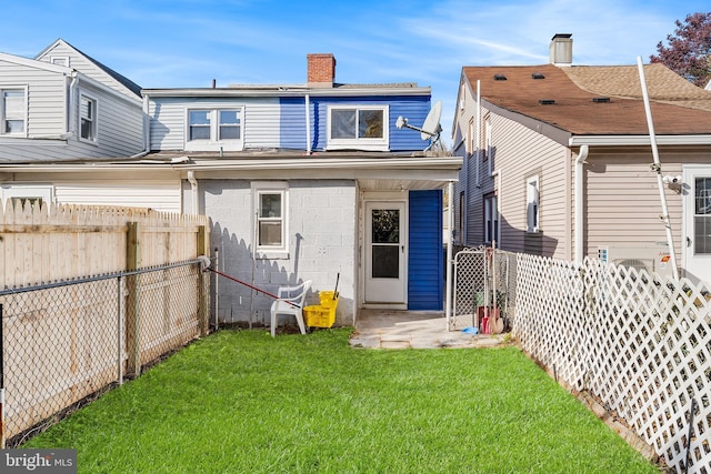 back of house with a lawn, a chimney, and a fenced backyard