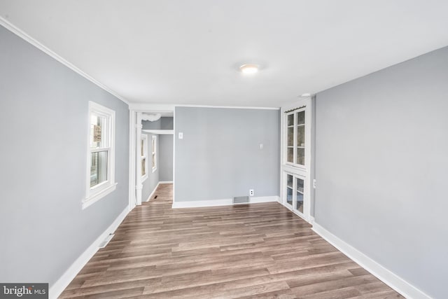 spare room with crown molding, baseboards, visible vents, and wood finished floors