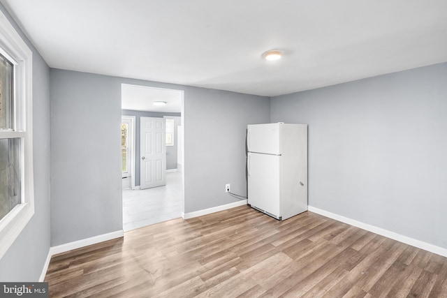 unfurnished bedroom with freestanding refrigerator, baseboards, and light wood-style floors