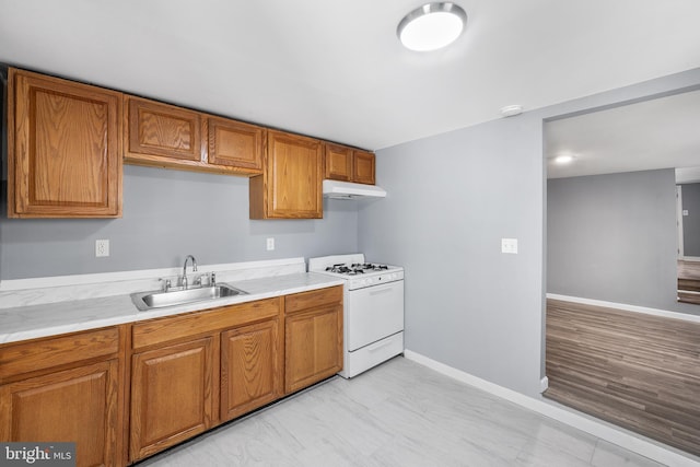 kitchen with brown cabinetry, a sink, light countertops, under cabinet range hood, and white gas range oven