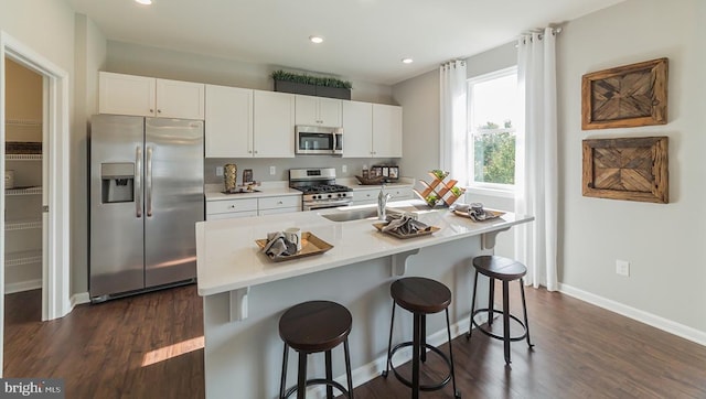 kitchen with appliances with stainless steel finishes, baseboards, white cabinets, a breakfast bar, and dark wood-type flooring