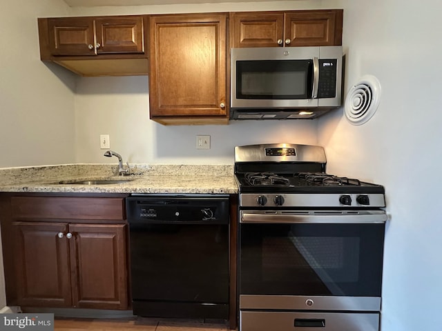 kitchen with a sink, appliances with stainless steel finishes, and light stone countertops