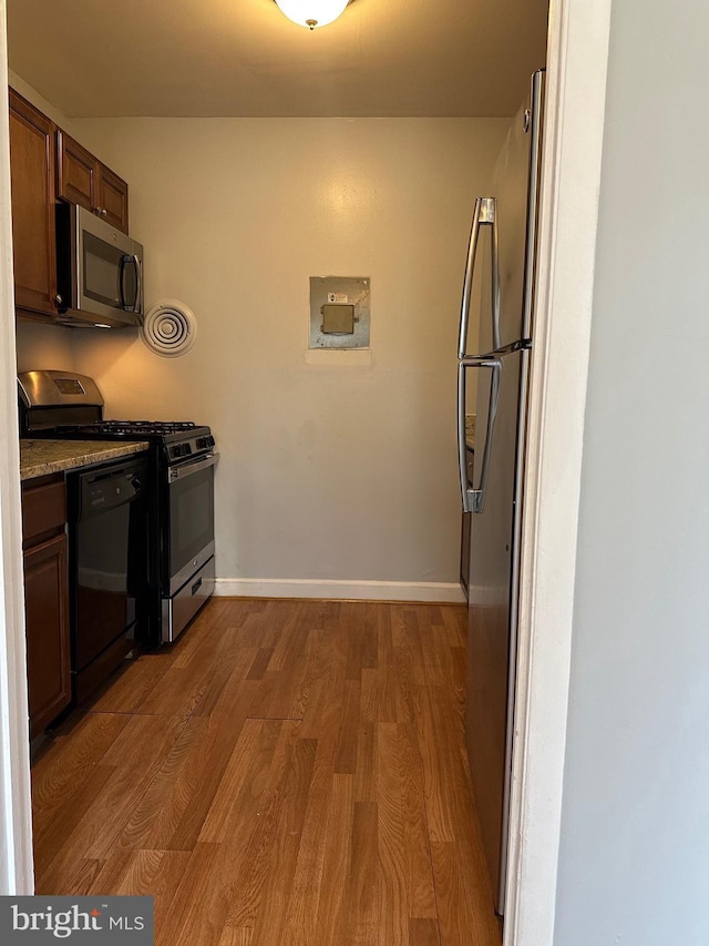 kitchen featuring baseboards, wood finished floors, and stainless steel appliances