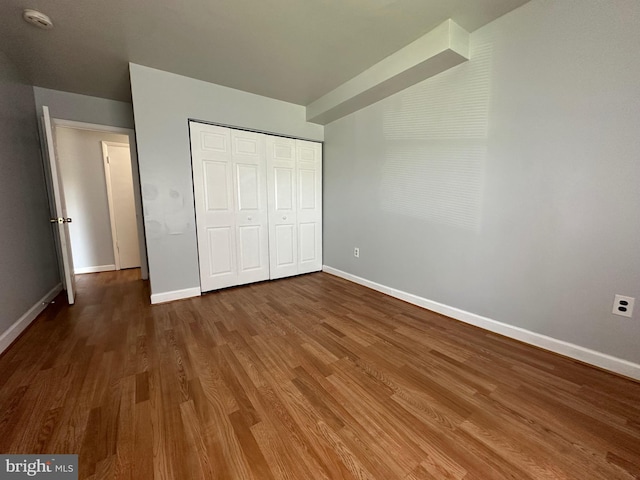 unfurnished bedroom with baseboards, a closet, and wood finished floors