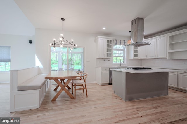 kitchen featuring white cabinets, a chandelier, decorative backsplash, island range hood, and light wood-type flooring