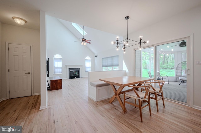 dining space with a glass covered fireplace, light wood-style floors, baseboards, high vaulted ceiling, and a skylight