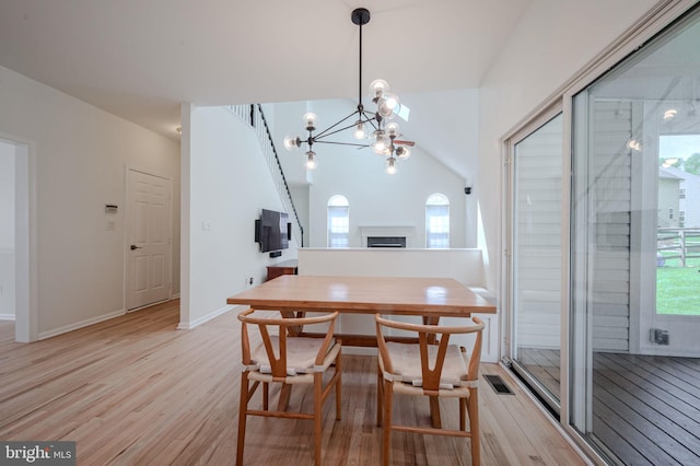 dining area featuring a notable chandelier, light wood finished floors, a fireplace, baseboards, and lofted ceiling