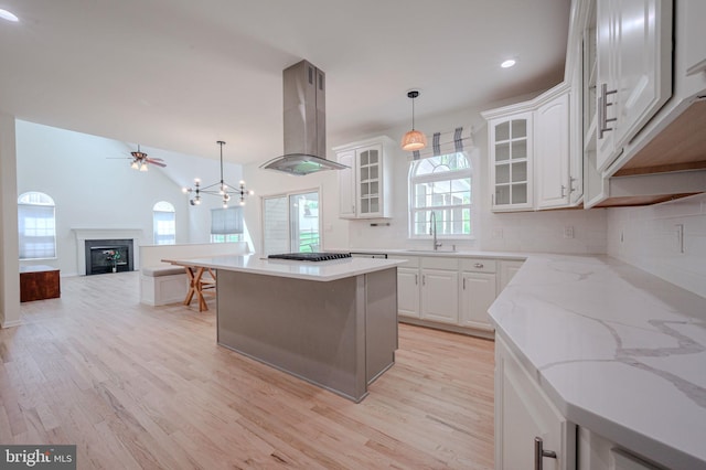 kitchen with gas cooktop, a sink, light wood finished floors, decorative backsplash, and island range hood
