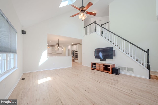 unfurnished living room with high vaulted ceiling, visible vents, stairway, and light wood-style floors
