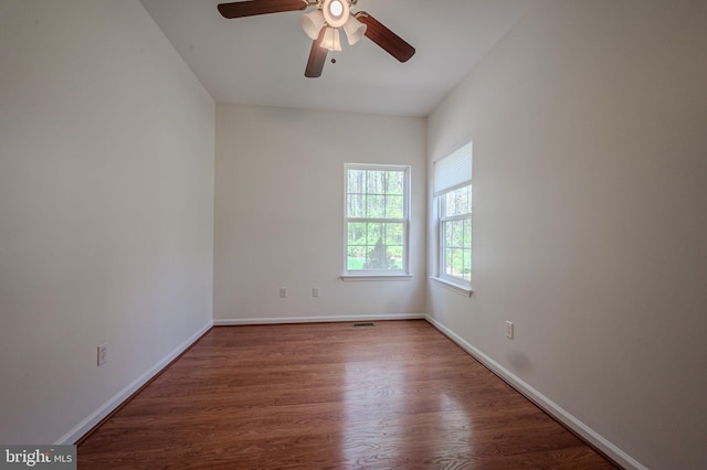 empty room featuring a ceiling fan, baseboards, visible vents, and wood finished floors