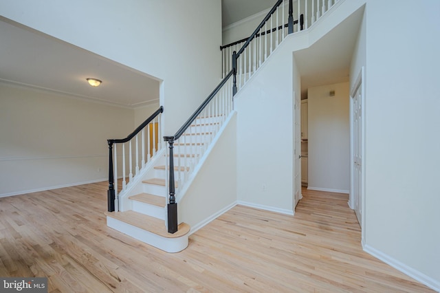 staircase with baseboards, ornamental molding, wood finished floors, and a high ceiling