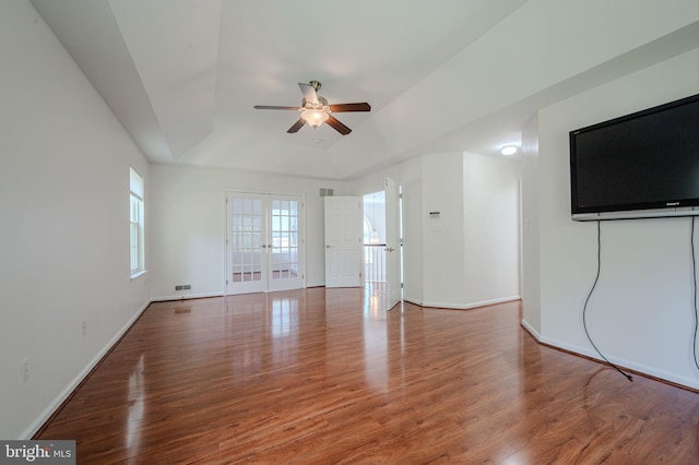 unfurnished living room featuring french doors, a ceiling fan, wood finished floors, a raised ceiling, and baseboards