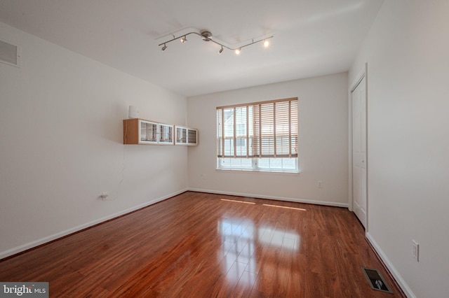 spare room with baseboards, visible vents, wood finished floors, and rail lighting