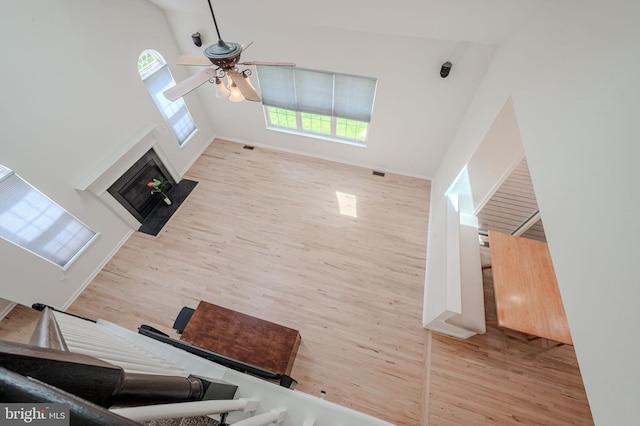 living area with a ceiling fan, a fireplace with flush hearth, wood finished floors, high vaulted ceiling, and baseboards