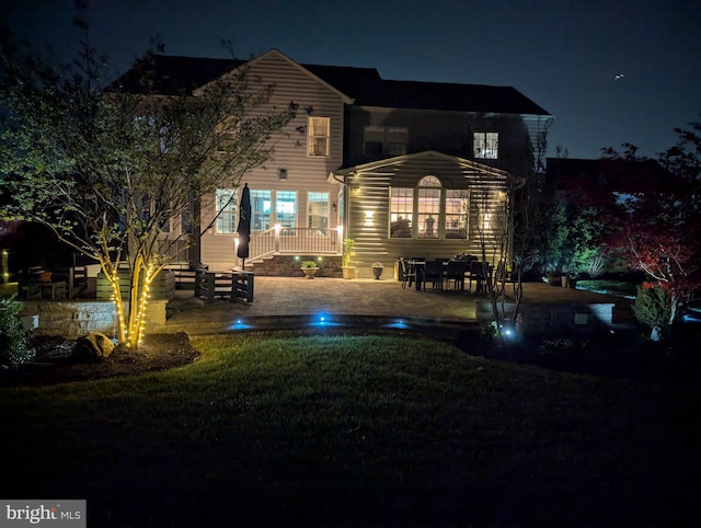 back of house at twilight featuring a lawn and a patio
